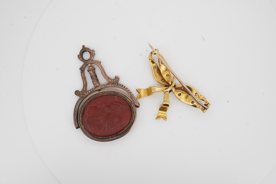 A yellow metal, seed pearl and diamond cluster seed ribbon bow brooch, width 36mm, gross weight 7.7 grams, together with a gilt metal and intaglio carnelian set spinning fob. Condition - poor to fair